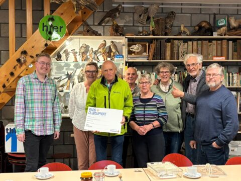 Een groep mensen poseert met een Rabo ClubSupport cheque in een ruimte met boeken en opgezette vogels.