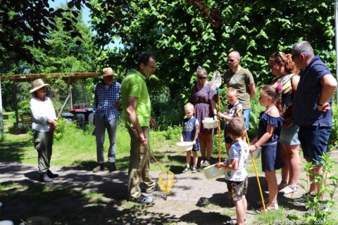 Groep mensen, waaronder kinderen, buiten met emmers en schepnetten, klaar voor natuuractiviteit.