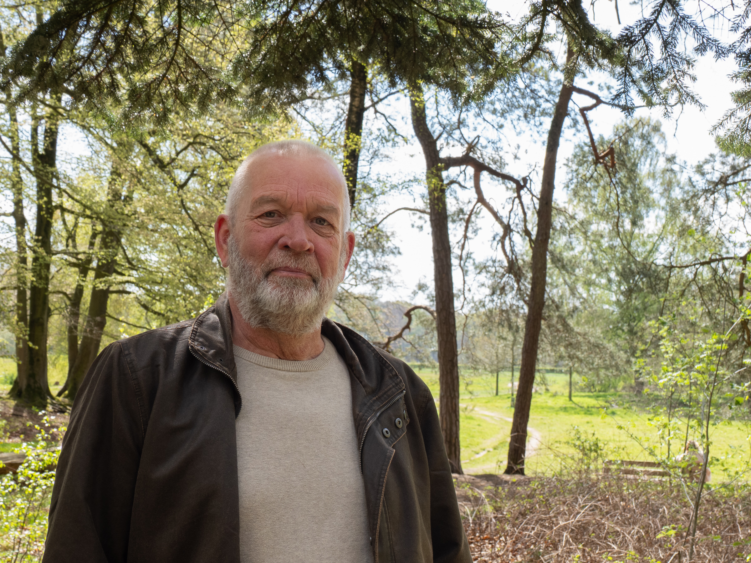 Man in bosrijke omgeving onder bomen, met een zonnige achtergrond.
