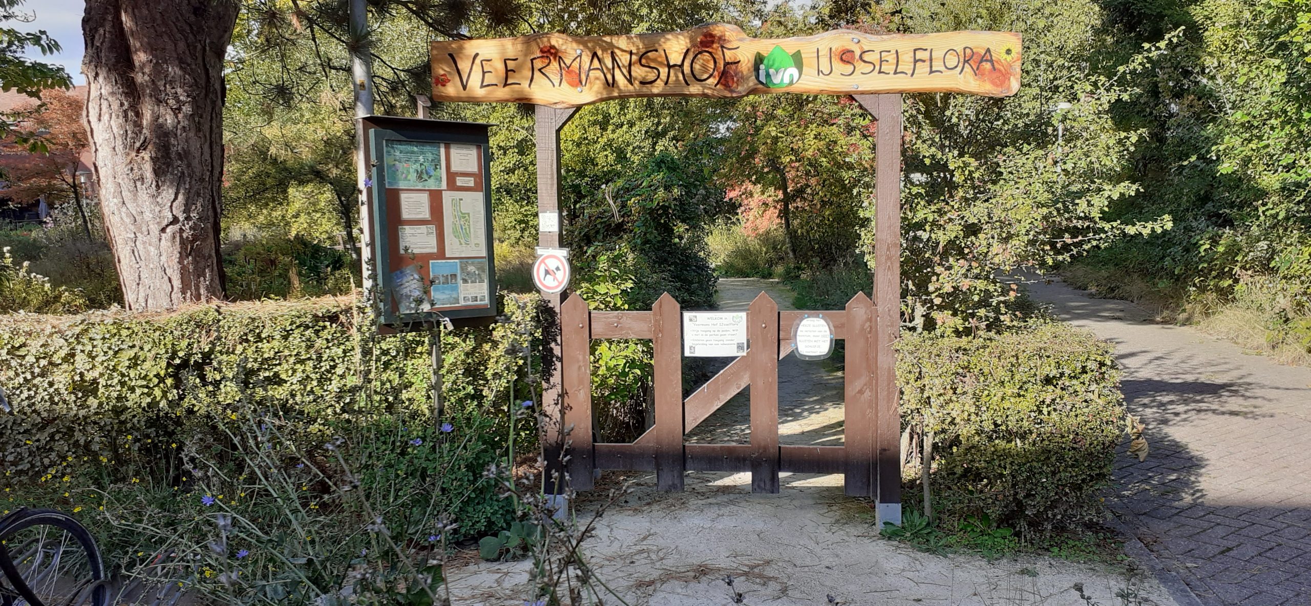 Toegangspoort naar Veermanshof IJsselflora omgeven door groen, informatiebord links.