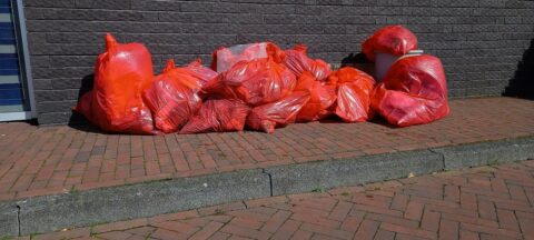 Rode vuilniszakken op een stenen trottoir naast een grijze muur.