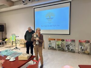 Een vrouw ontvangt een prijs bij een presentatie over historische bomen, omringd door natuurborden.