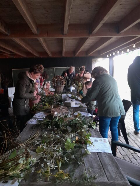 Mensen aan een tafel maken decoraties met bladeren en takken in een houten schuur.
