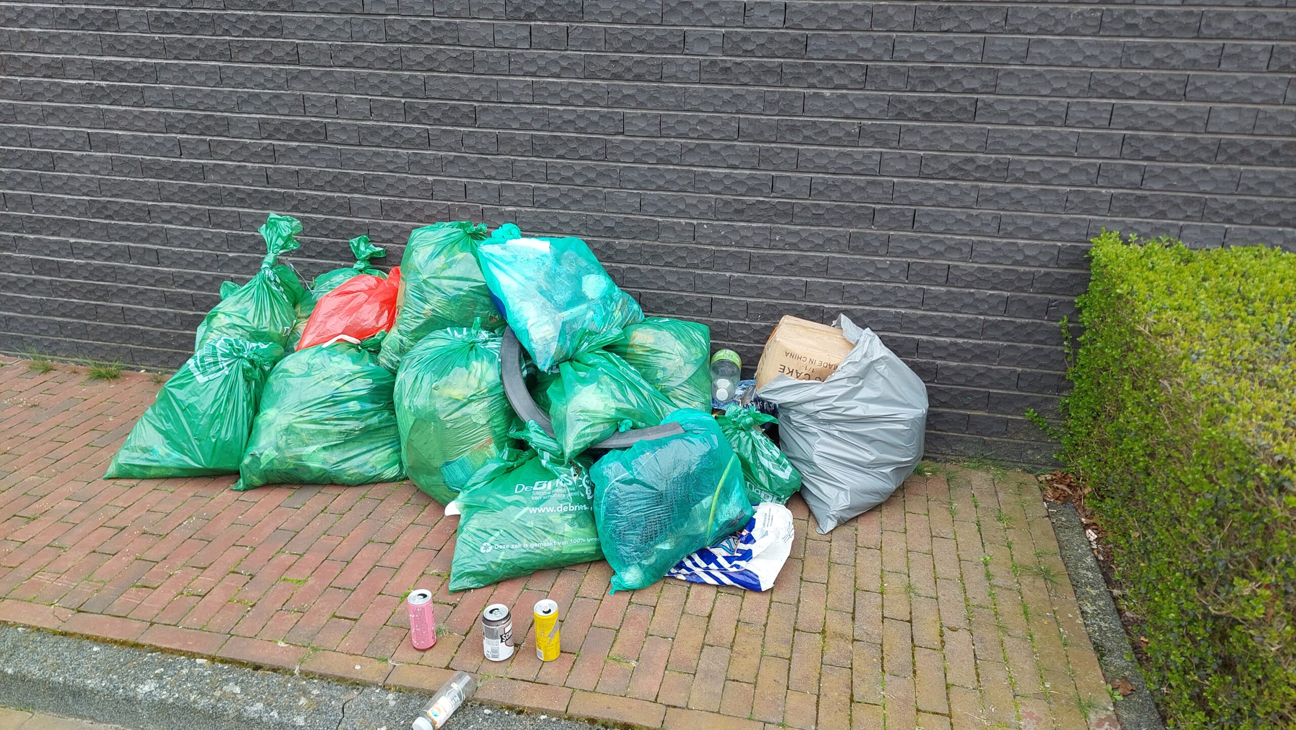Stapels vuilniszakken liggen op straat langs een muur en naast een heg.