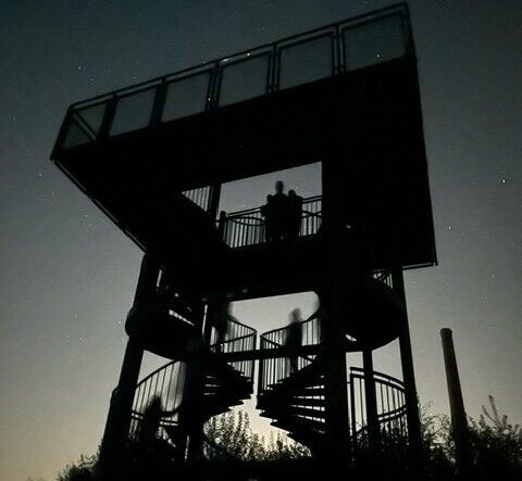 Silhouet van een uitkijktoren met mensen bij zonsondergang.