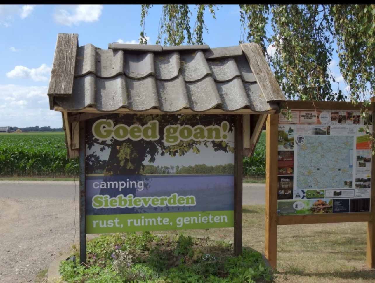 Bord bij camping met tekst "Goed goan!" en "Siebieverden". Naast bord een informatiepaneel en groene omgeving.