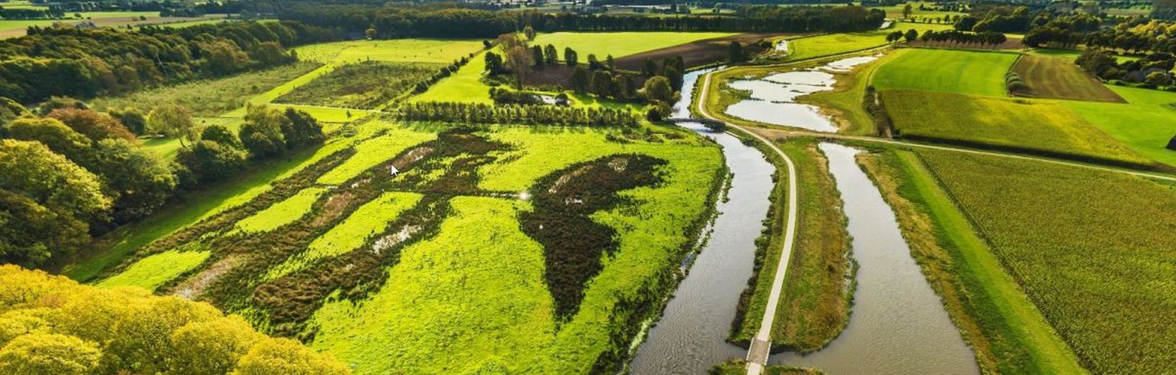 Luchtfoto van groen landschap met rivieren, boompartijen en open velden onder blauwe lucht.