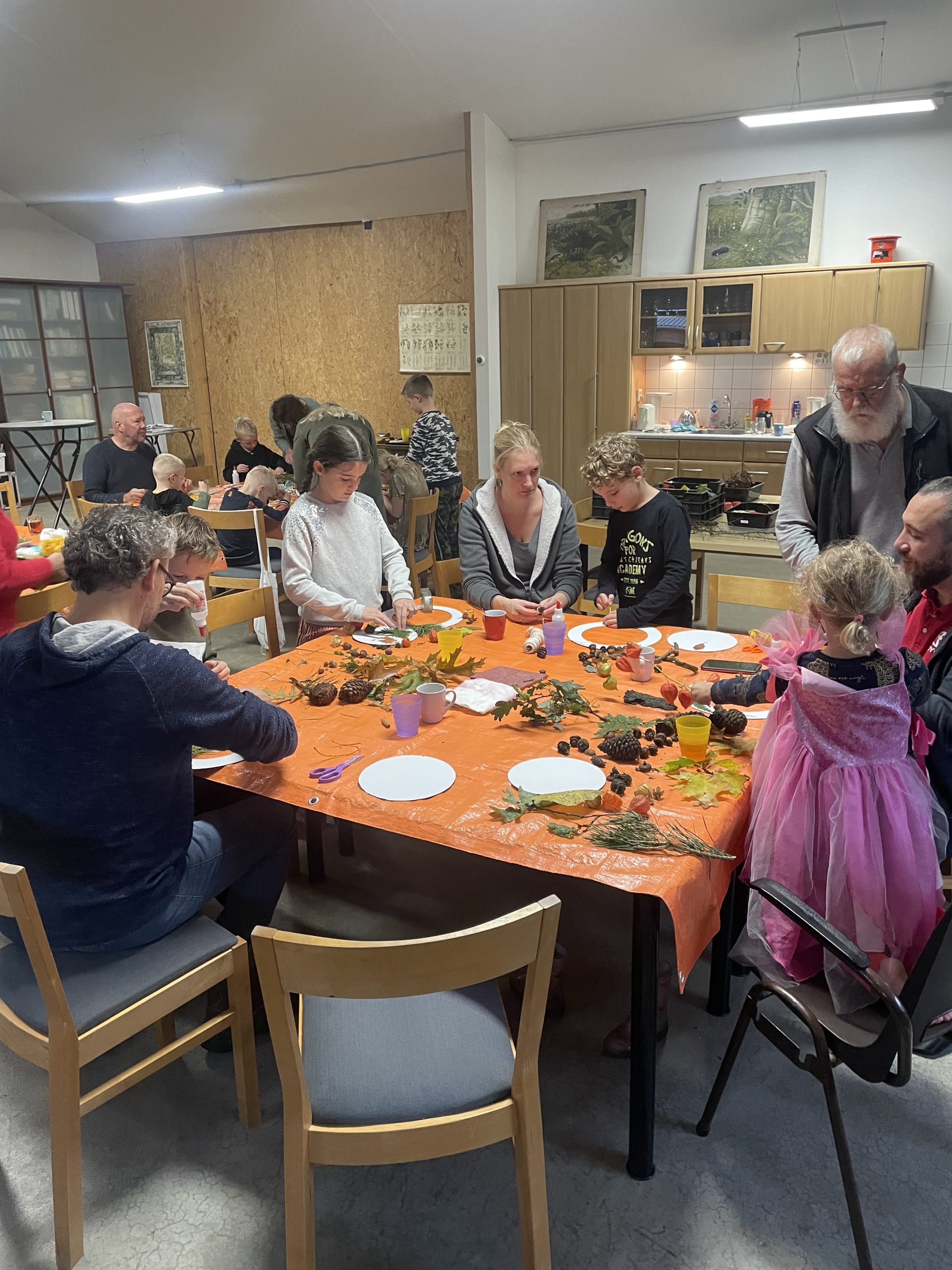 Mensen knutselen samen aan een tafel bedekt met bladeren, dennenappels en andere natuurelementen.