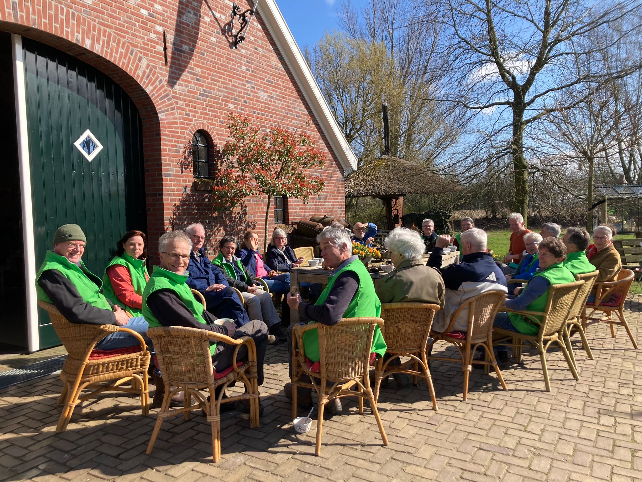 Groep mensen zit buiten rond tafels bij een boerderij, genietend van de zon.