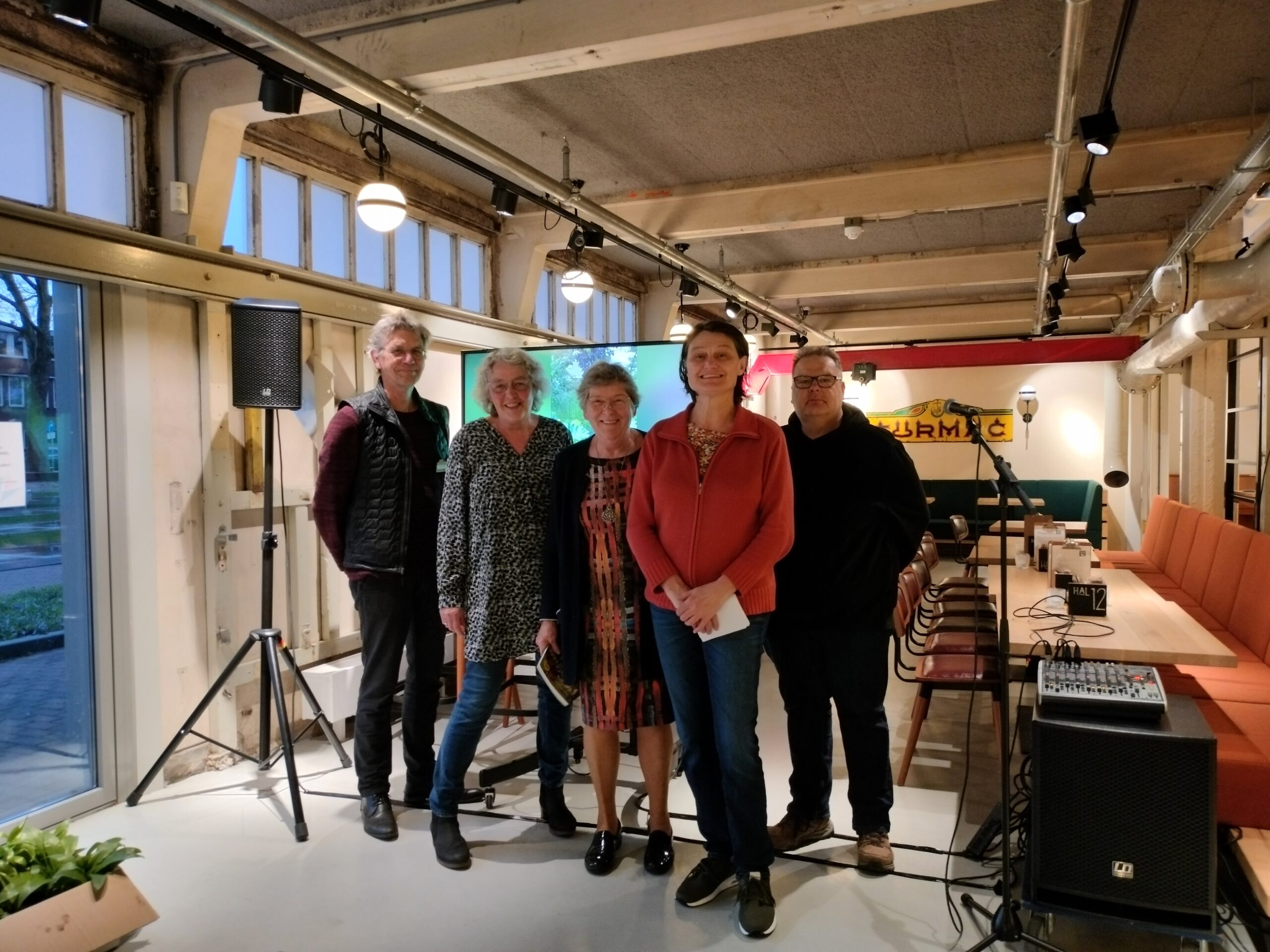 Groep van vijf mensen poseert in een moderne, lichte ruimte met audiovisuele apparatuur.