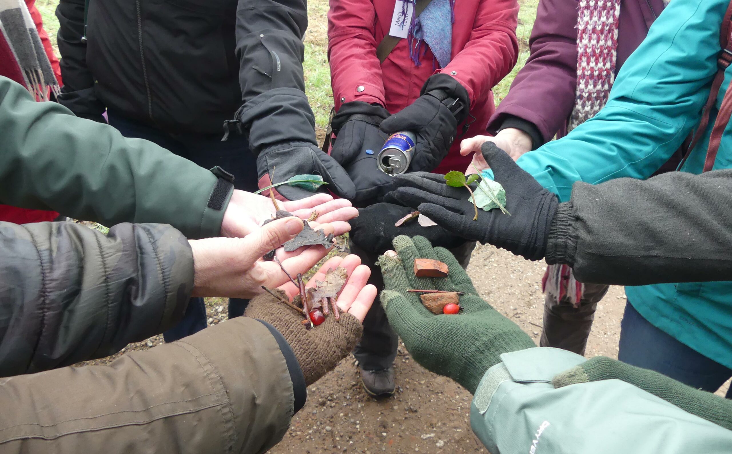 Groep mensen toont gevonden voorwerpen: bladeren, bakstenen en een blikje. Ze dragen handschoenen.