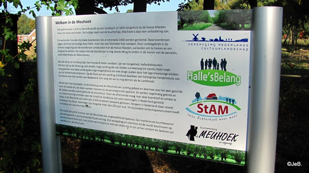 Informatiebord in bosgebied met tekst over Meuhoek en logo’s van lokale verenigingen.