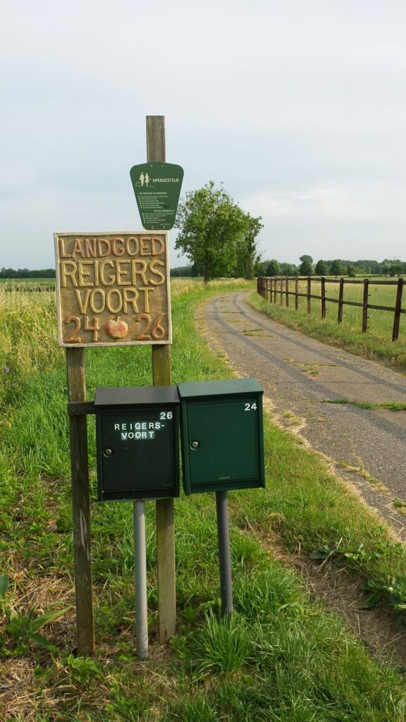 Bord bij Landgoed Reigersvoort met huisnummers, 24 en 26, naast een landweggetje en weilanden.