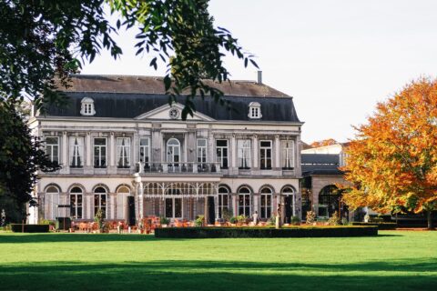 Elegant landhuis met veranda, omgeven door groene gazon en kleurrijke herfstbomen.