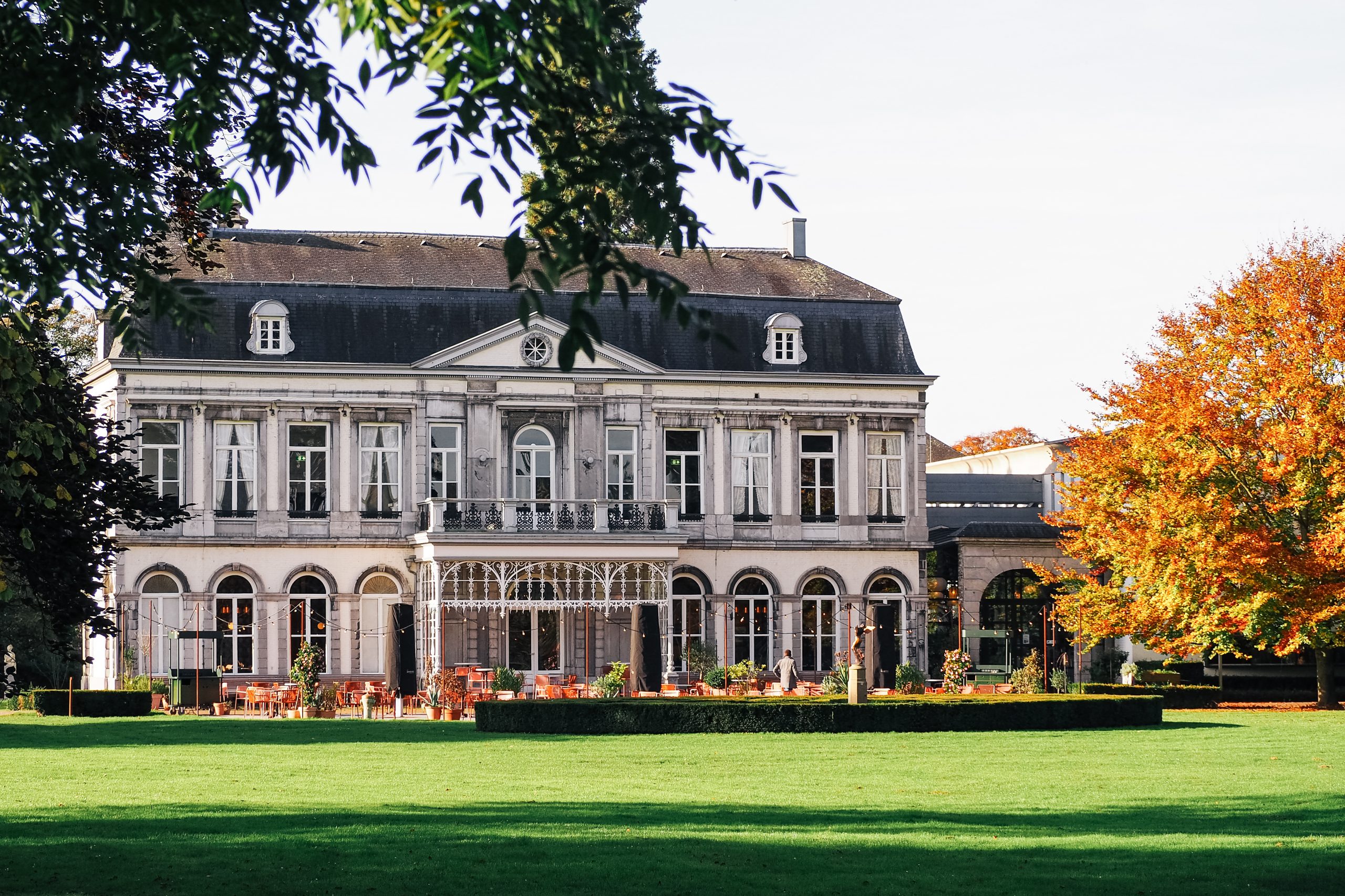 Elegant landhuis met veranda, omgeven door groene gazon en kleurrijke herfstbomen.