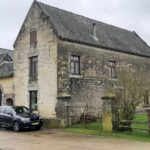 Oudhollandse boerderij met stenen muren, drie auto's en een hek op een bewolkte dag.