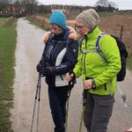 Twee wandelaars met wandelstokken op een landweg op een bewolkte dag.