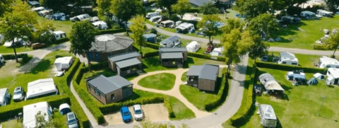Luchtfoto van een camping met huisjes, caravans en groene omgeving.