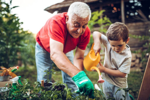 Opa en kleinzoon planten water geven in de tuin, beiden verdiept in hun taak.