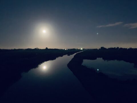 Volle maan reflecteert in een rustige rivier in een donkere, landelijke nacht.