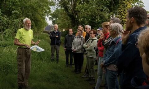 Een gids geeft uitleg aan een groep mensen op een groen, bosrijk pad.