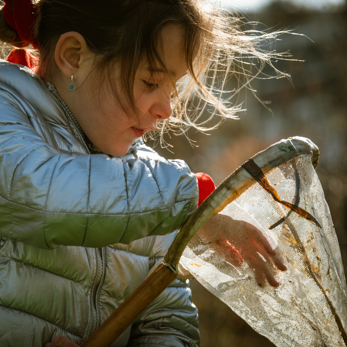 Kind in zilveren jas onderzoekt vangnet buiten in zonlicht.