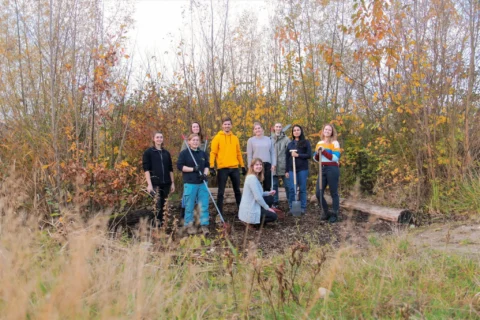 Groep mensen poseert in een herfstbos met gereedschap voor tuinwerk.