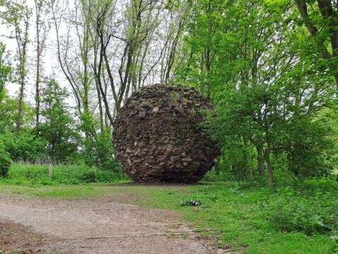 Een grote, ruige steenbol ligt in een bosrijke omgeving met dichte groene bomen.
