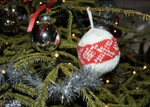 Kerstboom met gebreid ornament, spiegelbal en zilveren slinger.