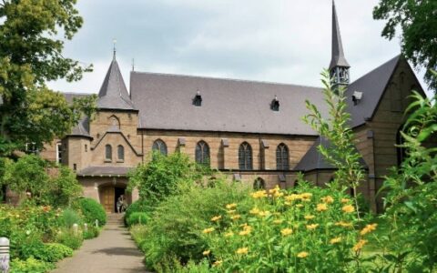 Middeleeuwse kerk omringd door een bloeiende tuin met een pad erdoorheen.