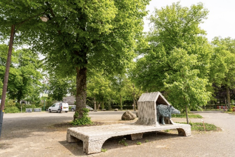 Park met houten kunstwerk, veel bomen en een geparkeerde witte bestelwagen.