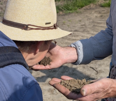 Twee mensen inspecteren en ruiken grond in hun handen buiten.
