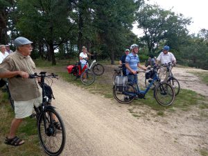 Een groep oudere volwassenen stopt met fietsen op een bosachtig pad.