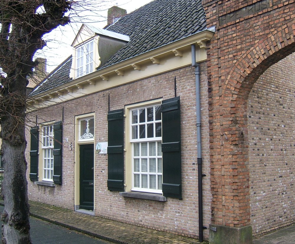 Bakstenen gebouw met groene luiken en een boogdoorgang, gelegen aan een geplaveide straat.