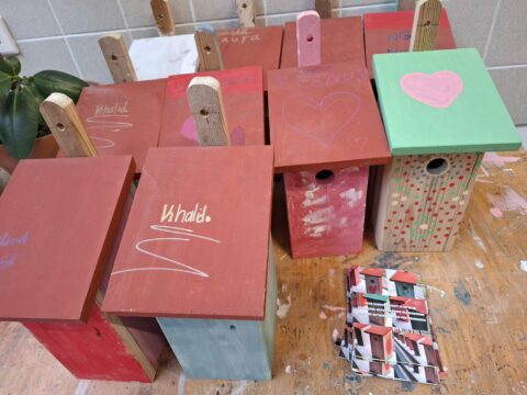 Gekleurde vogelhuisjes met namen en hartjes, op werkbank naast brochures.