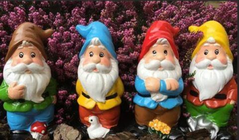 Vier kleurrijke kabouters staan naast elkaar voor een achtergrond van paarse bloemen.