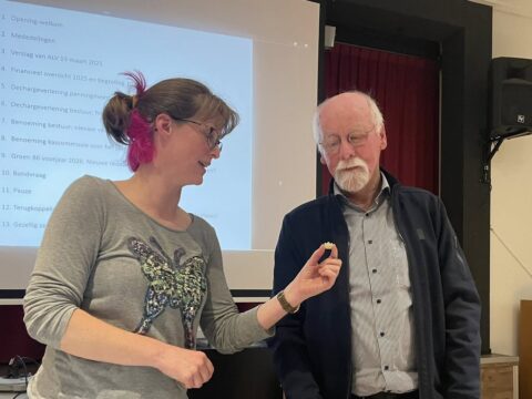 Twee mensen praten voor een projectiescherm met vergaderagenda.