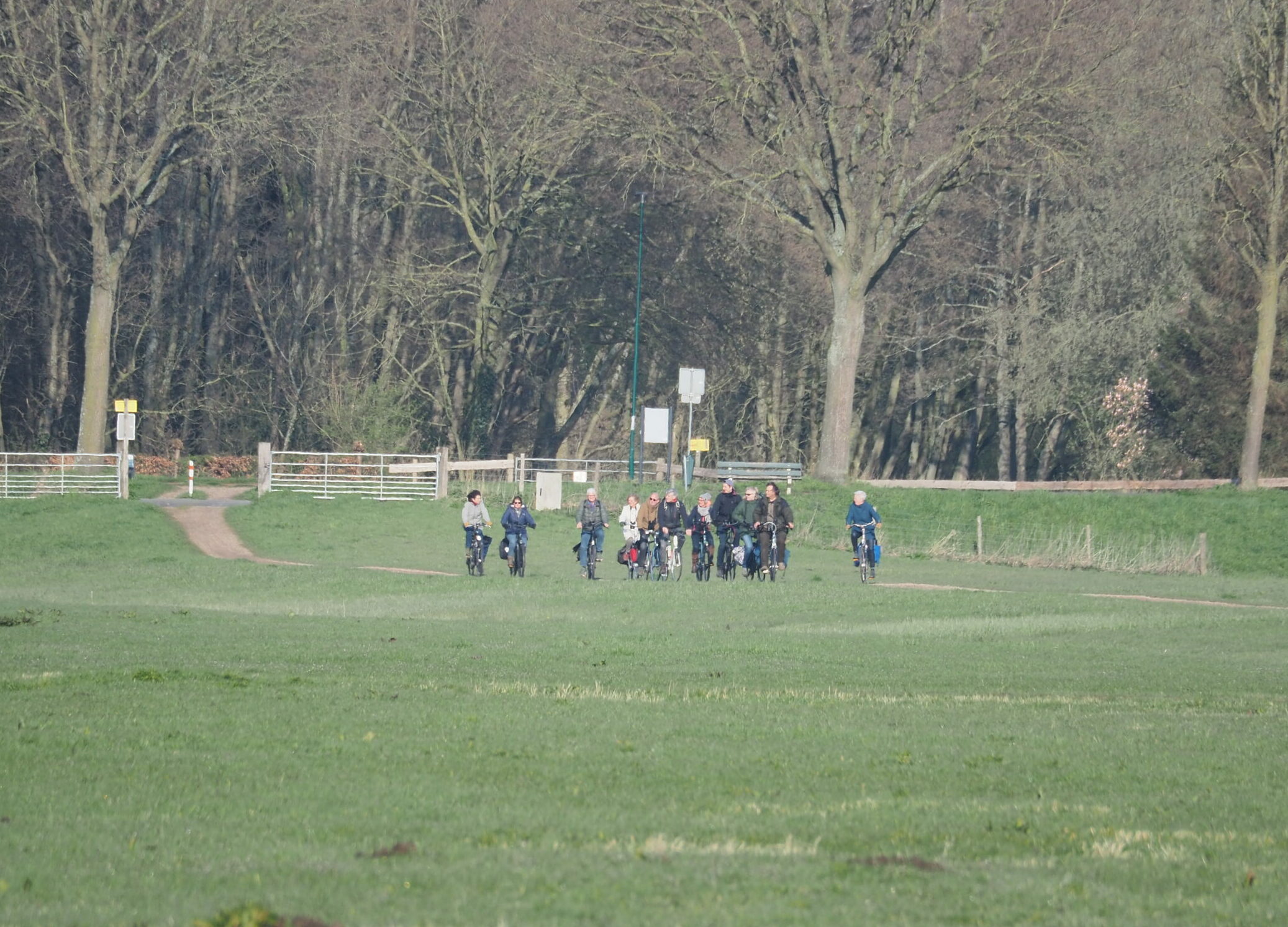 Groep fietsers op een pad in een groen park met bomen op de achtergrond.