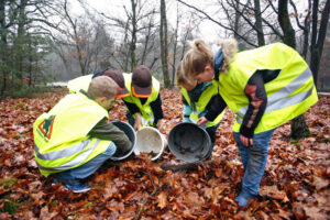 Kinderen in gele hesjes onderzoeken emmers in een herfstbos.