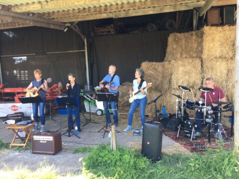 Een band speelt muziek in een schuur naast opgestapelde hooibalen.