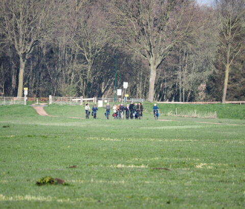 Een groep mensen fietst over een groen veld met bomen op de achtergrond.