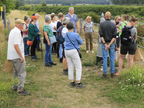 Groep mensen luistert naar een gids bij een natuurwandeling in een landelijke omgeving.