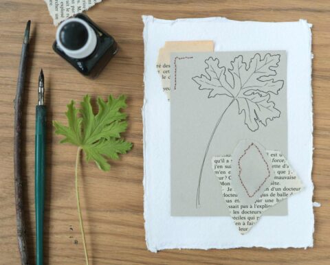 Inktfles, houten pen, groen blad en getekend blad op papier op houten tafel.