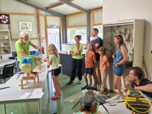 Een man legt insectenmodellen uit aan een groep mensen in een educatieve ruimte.