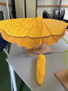Grote gele kunstvlinder en spinachtige sculptuur op tafel.