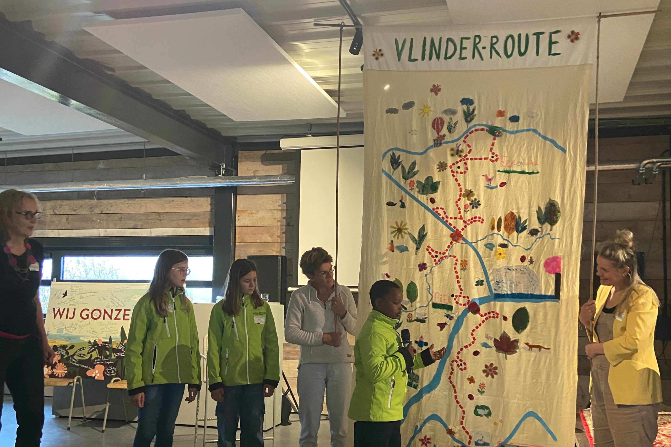 Een groep mensen presenteert een kleurrijke kaart van de "Vlinderroute" binnenshuis.