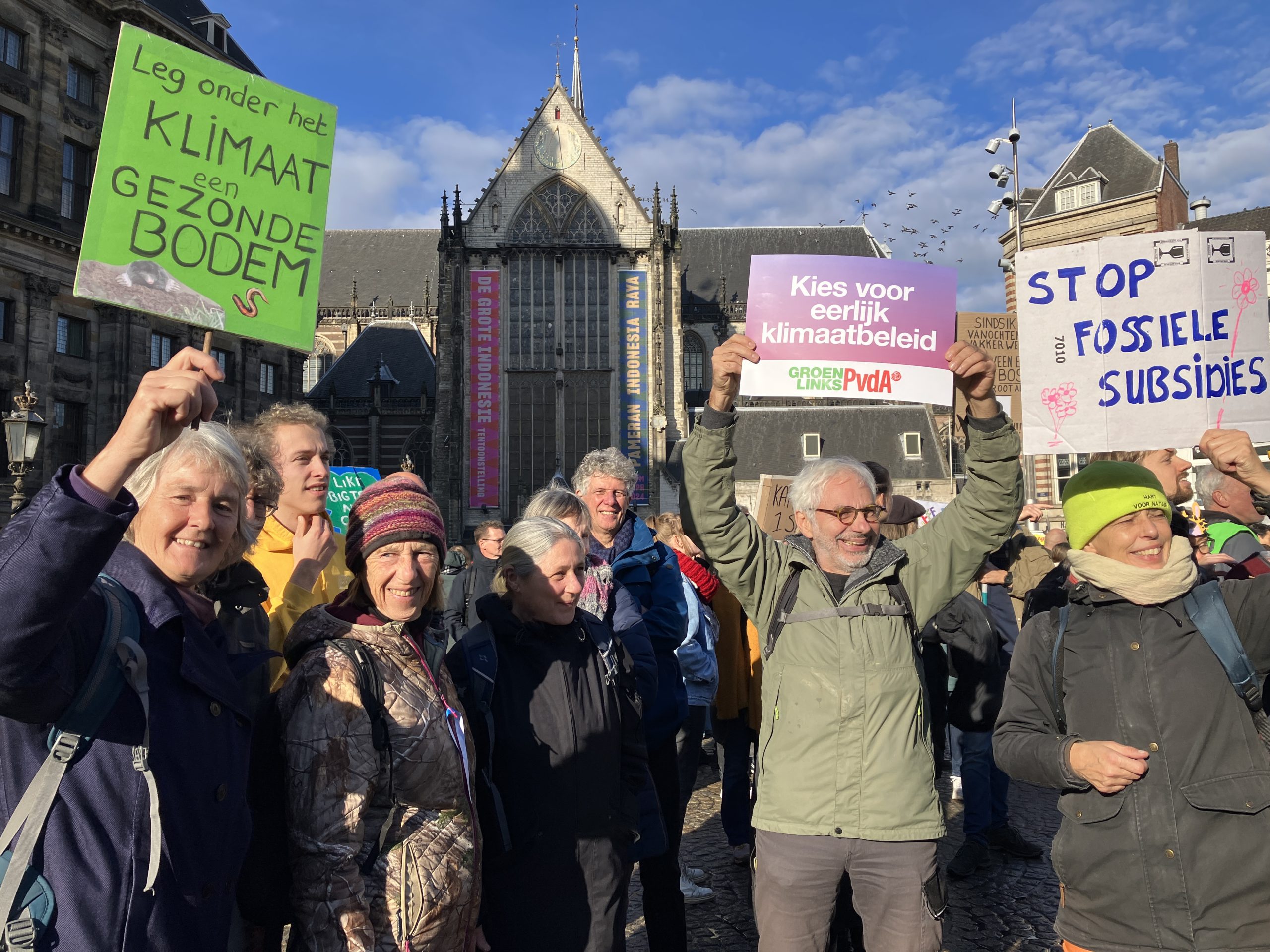 Demonstranten op de Dam in Amsterdam houden protestborden over klimaatbeleid omhoog.