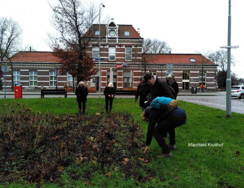 Groep mensen werkt in een tuin voor een historisch gebouw met klokgevel.