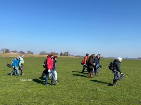 Groep mensen wandelt over een groen veld met afvalprikkers en vuilniszakken.
