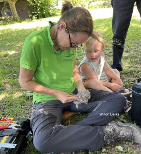 Vrouw met bril houdt een jonge uil vast op schoot terwijl een kind nieuwsgierig toekijkt.